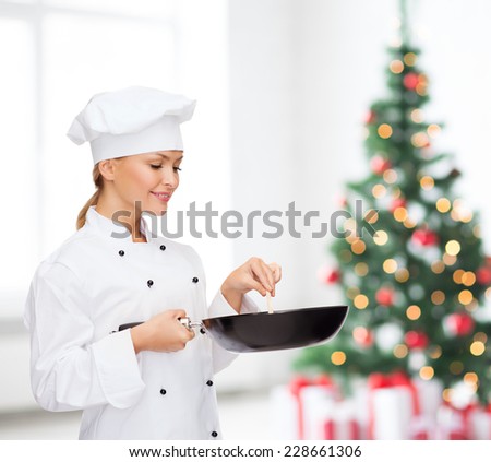 cooking, holidays, people and food concept - smiling female chef with pan and spoon mixing food over living room and christmas tree background