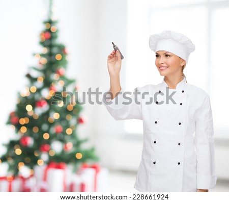 cooking, holidays, advertisement and people concept - smiling female chef, cook or baker with marker writing something on virtual screen over living room and christmas tree background