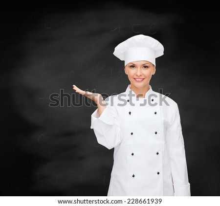 cooking, advertisement and people concept - smiling female chef, cook or baker holding something on palm of hand over blackboard background