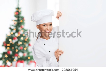 cooking, advertisement, holidays and people concept - smiling female chef, cook or baker with white blank board over living room and christmas tree background