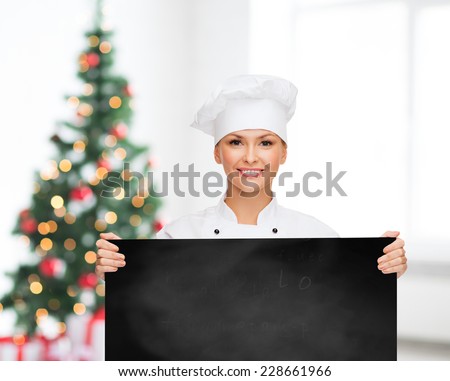 cooking, advertisement, holidays and people concept - smiling female chef, cook or baker with blank blackboard over living room and christmas tree background