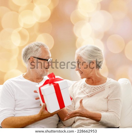 family, holidays, christmas, age and people concept - happy senior couple with gift box over beige lights background