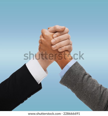 business, people, international and competition concept - close up of two hands multiracial armwrestling or handshake over blue background