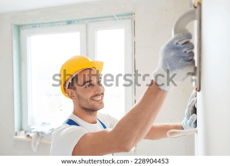 building, profession and people concept - smiling builder in hardhat sanding wall indoors