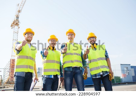 business, building, teamwork, technology and people concept - group of smiling builders in hardhats with tablet pc computer and clipboard showing thumbs up gesture outdoors