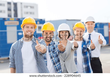 business, building, teamwork, gesture and people concept - group of smiling builders in hardhats showing thumbs up outdoors