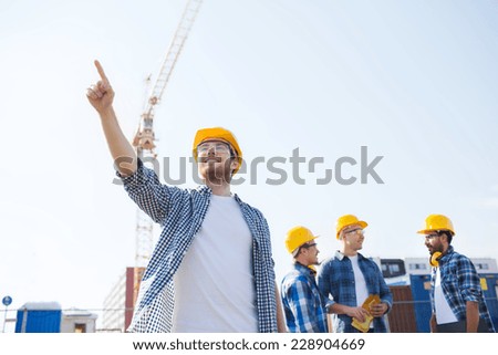 business, building, teamwork and people concept - group of smiling builders in hardhats pointing finger outdoors