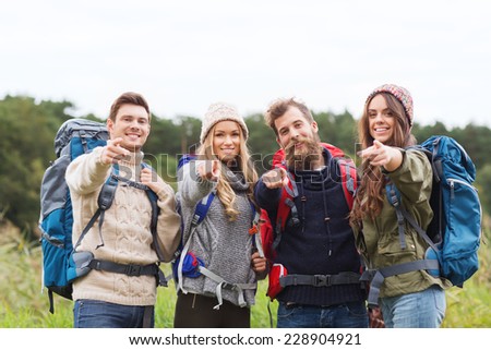 adventure, travel, tourism, hike and people concept - group of smiling friends with backpacks pointing finger outdoors