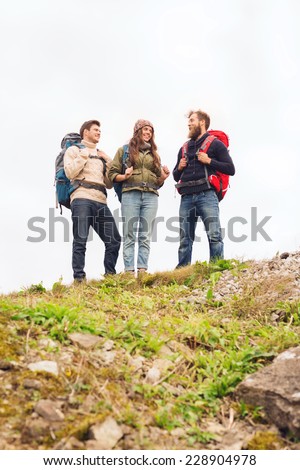 adventure, travel, tourism, hike and people concept - group of smiling friends with backpacks standing on hill and talking outdoors