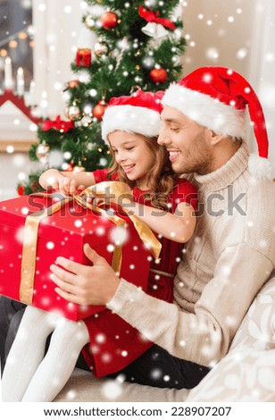 christmas, holidays, family and people concept - smiling father and daughter in santa hats holding gift box at home