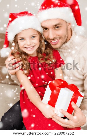 christmas, holidays, family and people concept - smiling father and daughter in santa hats holding gift box and hugging at home