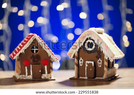 holidays, christmas, baking and sweets concept - closeup of beautiful gingerbread houses on table over blue garland lights