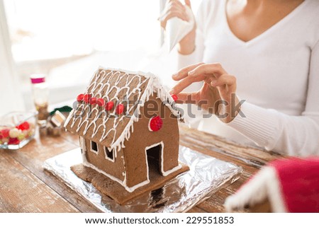 cooking, people, christmas and decoration concept - close up of happy woman making gingerbread houses at home