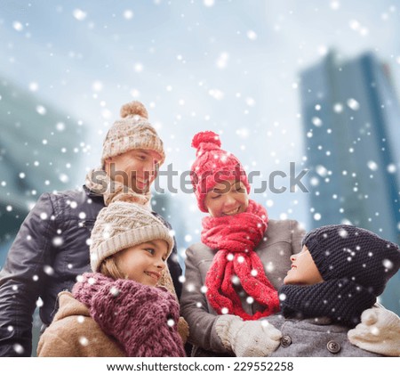family, childhood, season and people concept - happy family in winter clothes over snowy city background