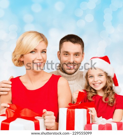 christmas, holidays, family and people concept - happy mother, father and little girl in santa helper hat with gift boxes over blue lights background