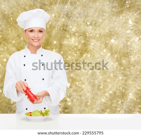 cooking, holidays, people and food concept - smiling female chef spicing vegetable salad over yellow lights background
