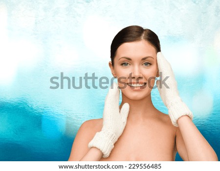 beauty, winter, people and health concept - smiling young woman in white mittens over blue glass background