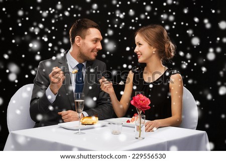 food, christmas, holidays and people concept - smiling couple eating dessert at restaurant over black snowy background