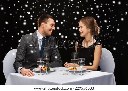 food, christmas, holidays and people concept - smiling couple eating main course at restaurant over black snowy background