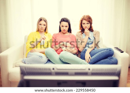 home, technology and friendship concept - three sad teenage girl watching tv at home and eating popcorn