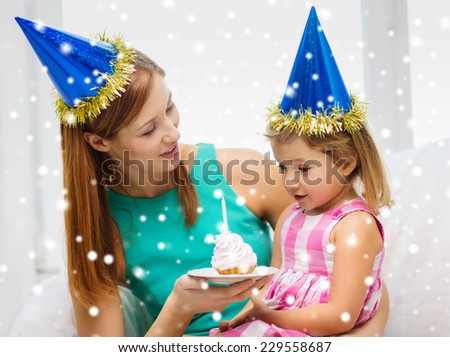 family, childhood, holidays and people concept - happy mother and daughter in blue party hats with cake and candle