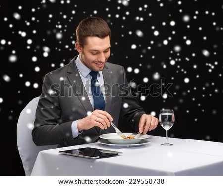 food, people, technology and holidays concept - smiling man with tablet pc eating main course at restaurant over black snowy background