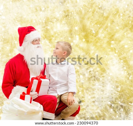 holidays, christmas, childhood and people concept - smiling little boy with santa claus and gifts over yellow lights background