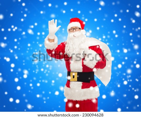 christmas, holidays, gesture and people concept - man in costume of santa claus with bag waving hand over blue snowy background