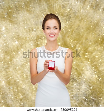 wedding, love, engagement and people concept - smiling woman in white dress holding red gift box with diamond ring over yellow lights background