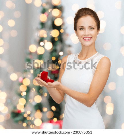 winter holidays, presents and people concept - smiling woman in white dress holding red gift box with diamond ring over christmas tree lights background