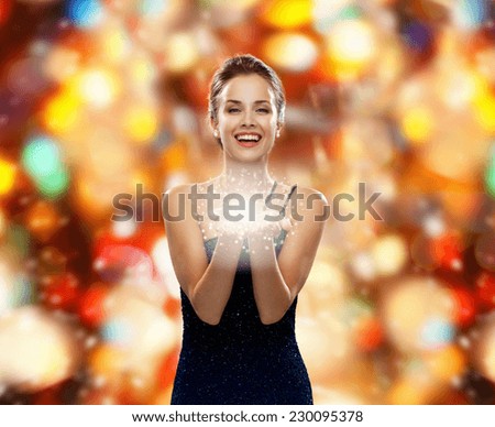 winter holidays, christmas and people concept - laughing woman in evening dress holding something over red lights background