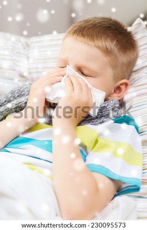 childhood, healthcare and people concept - ill boy with flu blowing nose into tissue at home