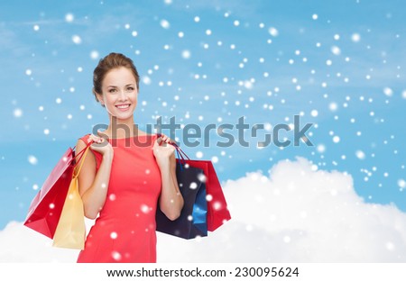 shopping, sale, christmas and holiday concept - smiling elegant woman in red dress with shopping bags over blue sky with cloud and snow background