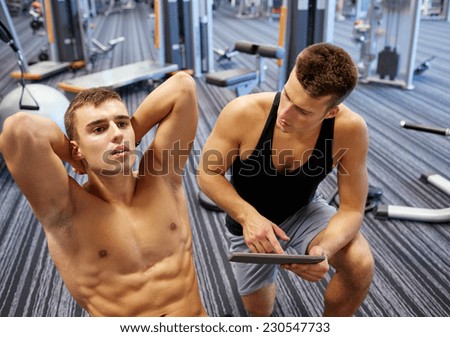 sport, fitness, lifestyle, technology and people concept - man and personal trainer with tablet pc computer and flexing abdominal muscles in gym