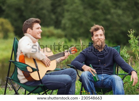 adventure, travel, tourism, friendship and people concept - smiling tourists playing guitar and drinking beer in camping