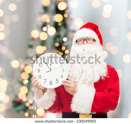 christmas, holidays and people concept - man in costume of santa claus with clock showing twelve over tree lights background