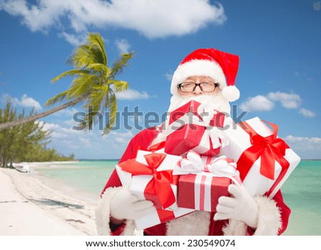 christmas, holidays and people concept - man in costume of santa claus with gift boxes over tropical beach background