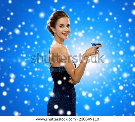drinks, winter holidays, christmas, luxury and celebration concept - smiling woman in evening dress holding cocktail over blue snowy background