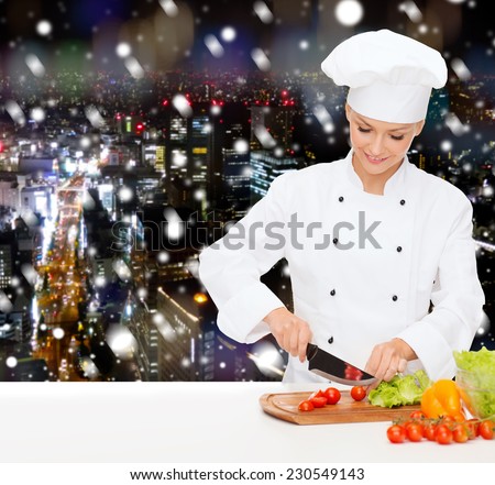 cooking, holidays, people and food concept - smiling female chef chopping vegetables over snowy night city background