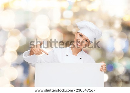 cooking, advertisement and people concept - smiling female chef, cook or baker pointing finger to white blank board over holidays lights background