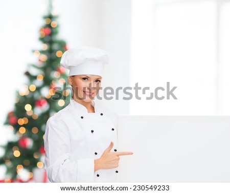 cooking, advertisement, holidays and people concept - smiling female chef, cook or baker pointing finger to white blank board over living room and christmas tree background
