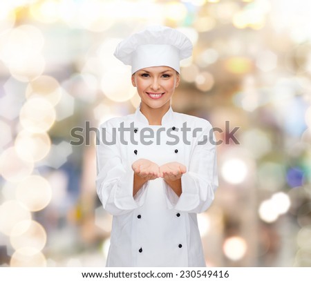 cooking, advertisement and people concept - smiling female chef, cook or baker holding something on palms of hands over holidays lights background