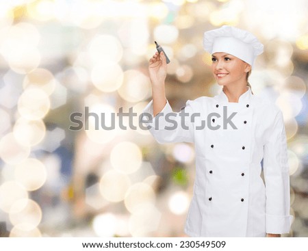 cooking, advertisement and people concept - smiling female chef, cook or baker with marker writing something on air over holidays lights background
