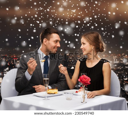 food, christmas, holidays and people concept - smiling couple eating dessert at restaurant over snowy night city background