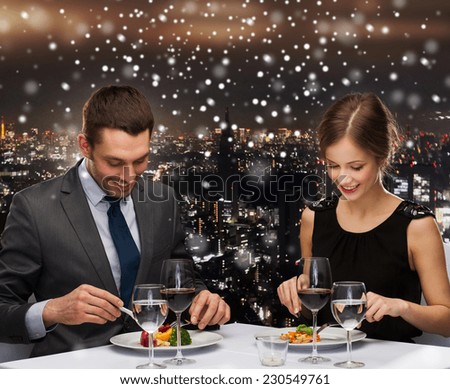food, christmas, holidays and people concept - smiling couple eating main course at restaurant over snowy night city background