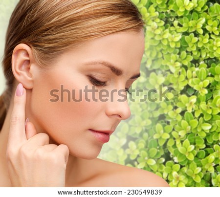 beauty, people and ecology concept - beautiful young woman touching or pointing finger to ear over green background