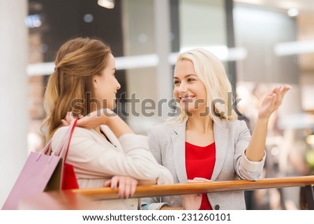 sale, consumerism and people concept - happy young women with shopping bags talking in mall