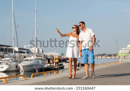 love, travel, tourism, sailing, people and friendship concept - smiling couple wearing sunglasses walking at harbor and pointing finger