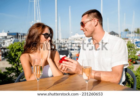 love, dating, people and holidays concept - smiling couple wearing sunglasses with champagne and small red gift box looking to each other at cafe