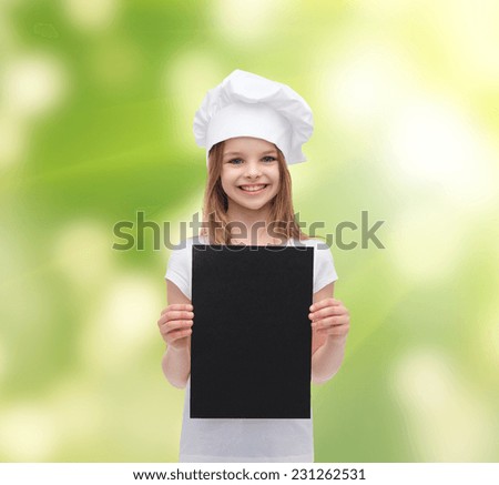 cooking, childhood, ecology, advertisement and people concept - smiling little chef girl or baker with blank black paper over green background